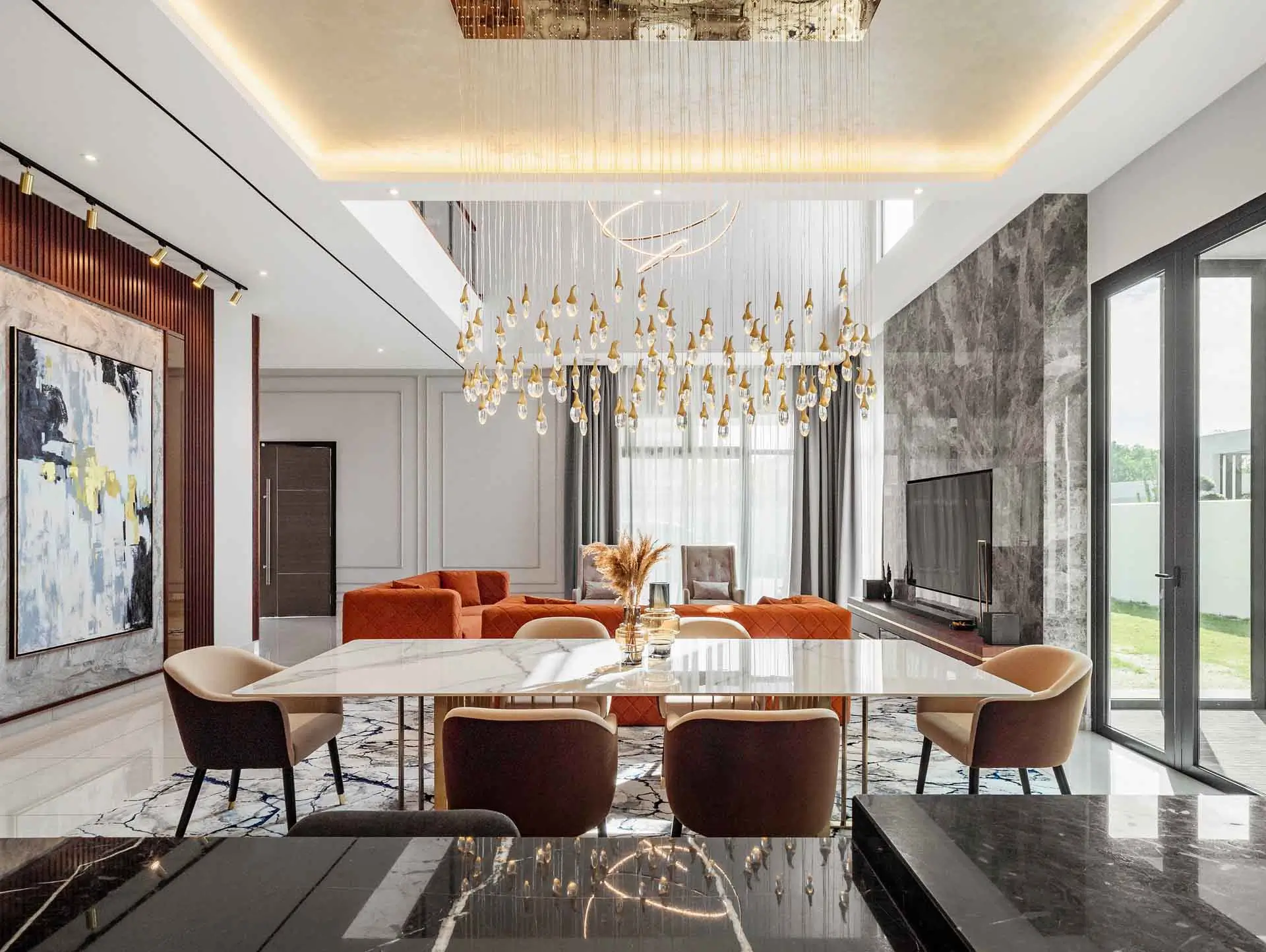 Open-plan dining area under a crystal-drop chandelier in a double-height void, opening to the living room, Setia Tropika bungalow, Johor Bahru, Malaysia, by Blaine Robert Design