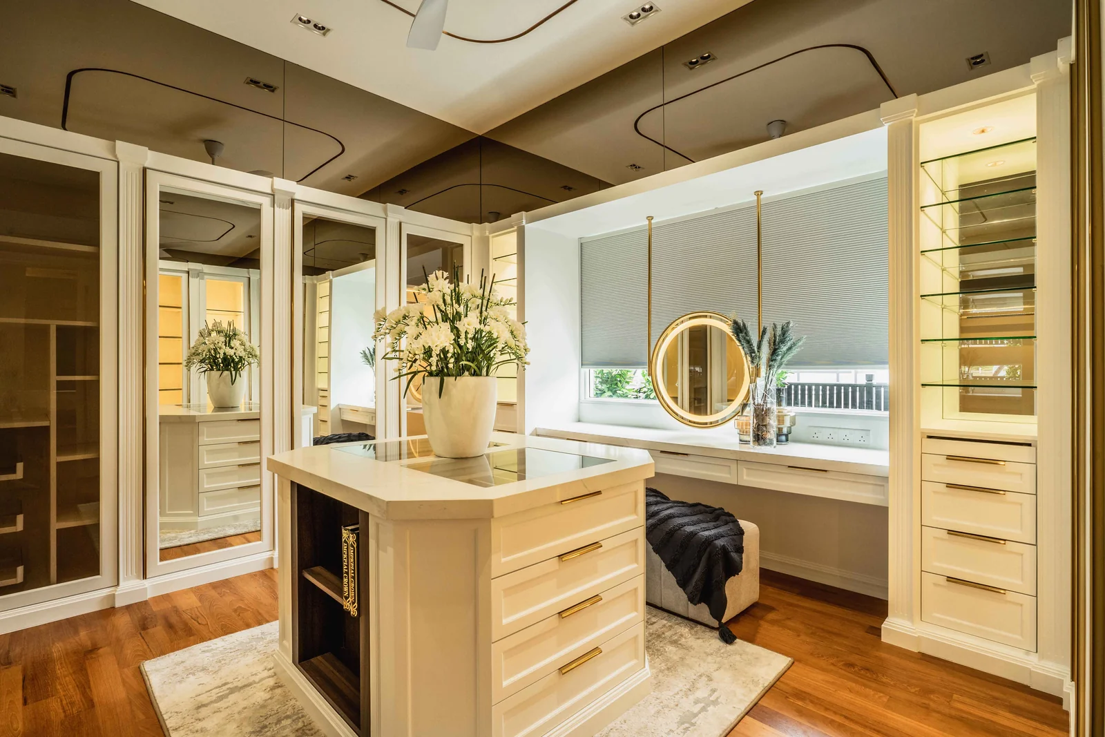 Walk in wardrobe with a central island, lit glass display cabinets and a dressing table under a round mirror, a bungalow at Eco Spring, Johor Bahru, Malaysia, by Blaine Robert Design